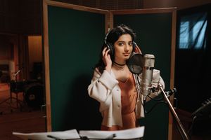A female musician recording vocals in a professional music studio.
