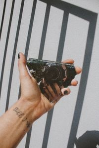 Artistic photo of a hand holding broken glass reflecting a camera with shadowed patterns.