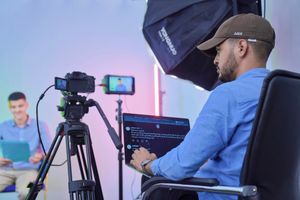 Man operates camera and laptop during a studio video shoot with a host and camera crew.