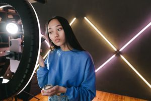Woman applying makeup under ring light in modern indoor setting, perfect for beauty content creators.